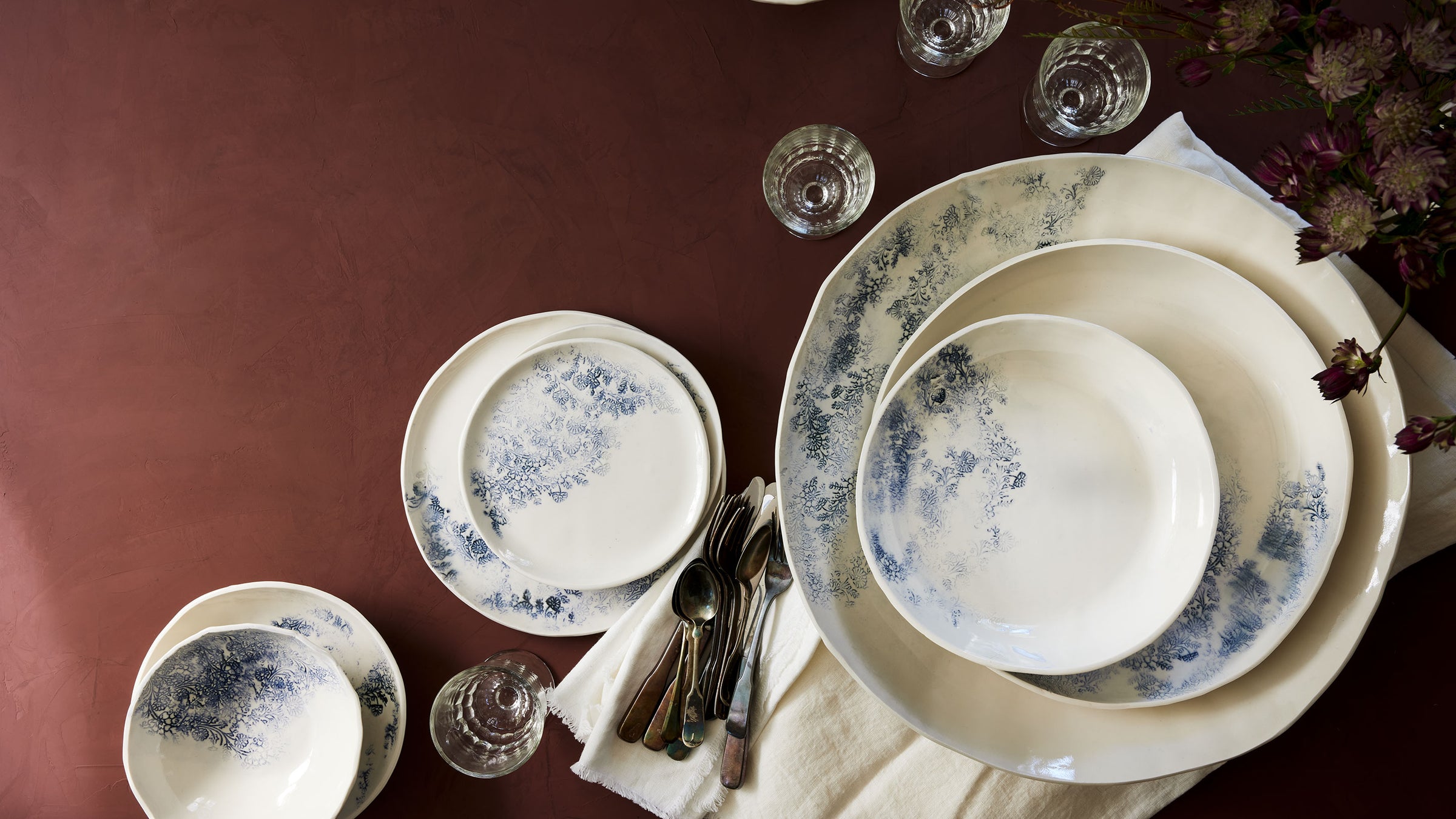 dbo home luxury ceramic dinnerware set in indigo kashmir woodblock pattern on rust tabletop with white linen and vintage glasses