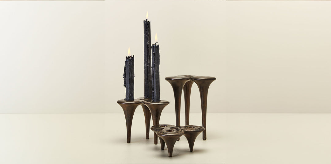 Cluster of three hand-cast bronze candlesticks from DBO Home with three lit black candles on a neutral background