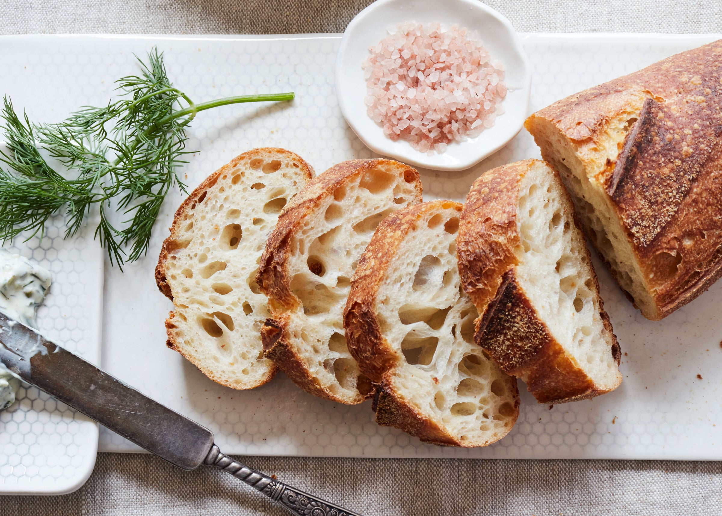 Freshly cut slices of crusty sourdough bread from Bourke Street Bakery on DBO Honeycomb Rectangular Serveware with a sprig of fresh dill and a vintage DBO dipping bowl full of pink Himalayan sea salt