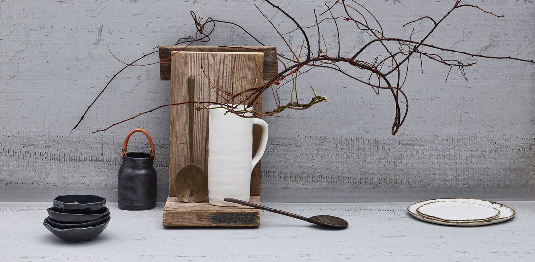 Magical Winter Minimalism Tastemakers Table by Kate McCann and David Prince, featuring minimalist white ceramic pitcher and black ceramic bowls on concrete background with wood and branches