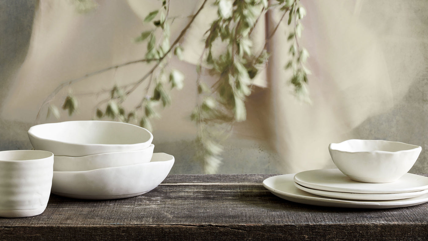 DBO HOME Ceramics | artisan bare white plates, bowls, and tumbler cup on natural wooden table with soft plant background
