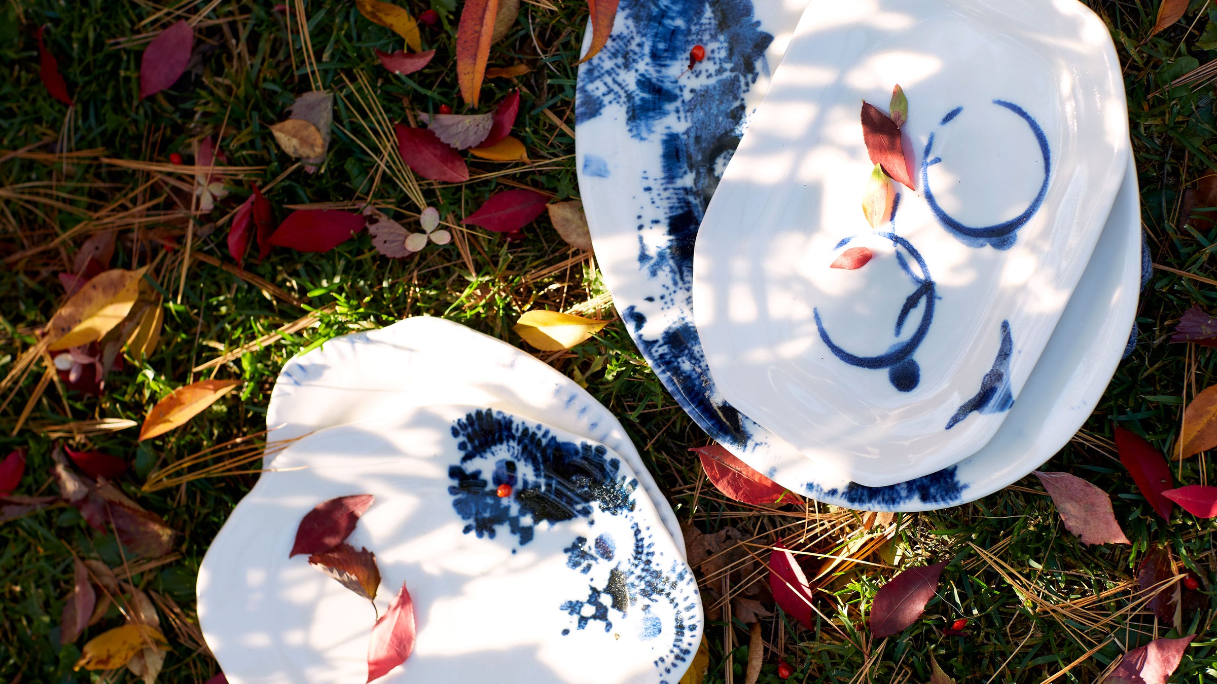 DBO HOME one of a kind handmade ceramic plates with indigo glaze on sunny autumn grass with leaves and pine needles