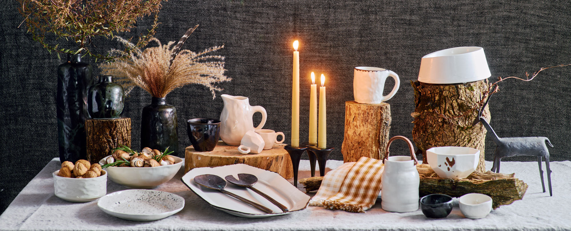 DBO HOME 2023 holiday gift guide spread of everyday luxury handmade ceramic and bronze pieces arranged on an elegant and rustic holiday table with lit candles and wood details