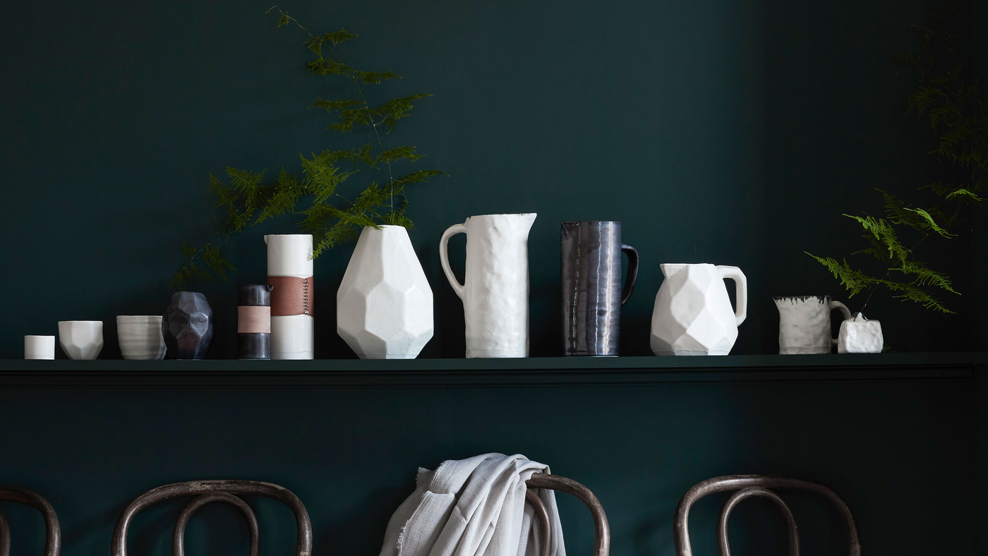 White and black textured artisan ceramics on shelf against teal wall with plants