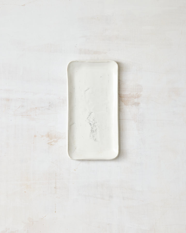 A small handmade porcelain plate from DBO Home's Birch collection, featuring a Salt n Pepper glaze and birch bark-impressed texture, photographed overhead on a white painted wood surface