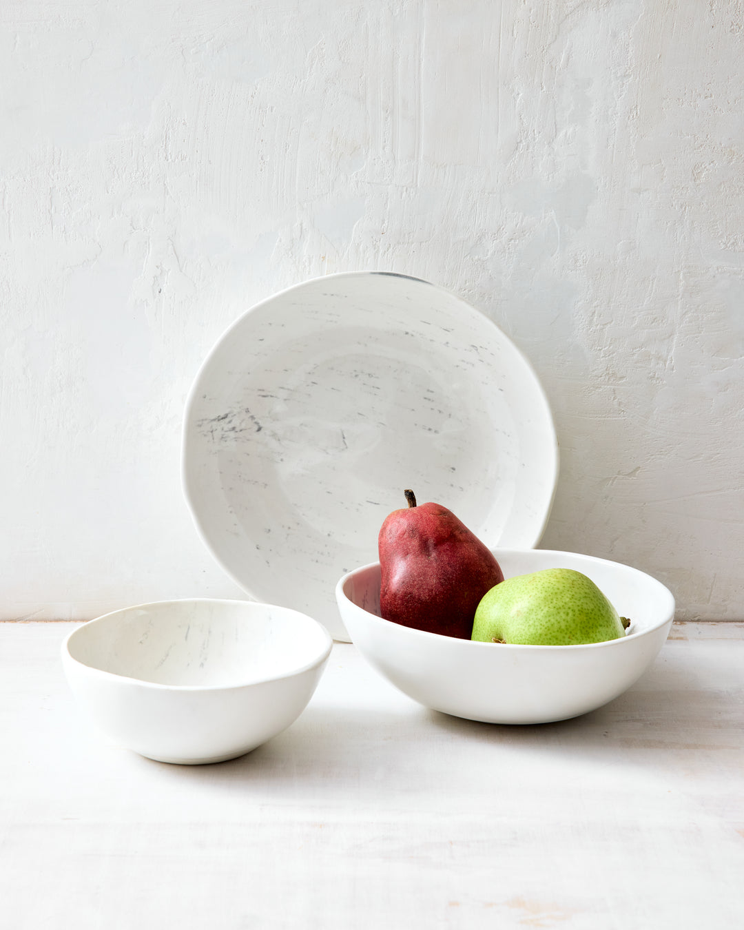 Three artisan ceramic bowls from DBO Home's Birch collection styled together — a small Soup Bowl, a medium Noodle Bowl holding two pears, and a large Everything Bowl propped upright — all in Salt n Pepper glaze with birch bark-impressed porcelain texture