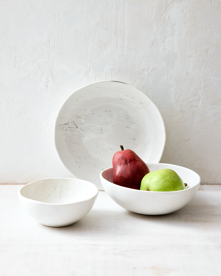 Three artisan ceramic bowls from DBO Home's Birch collection styled together — a small Soup Bowl, a medium Noodle Bowl holding two pears, and a large Everything Bowl propped upright — all in Salt n Pepper glaze with birch bark-impressed porcelain texture