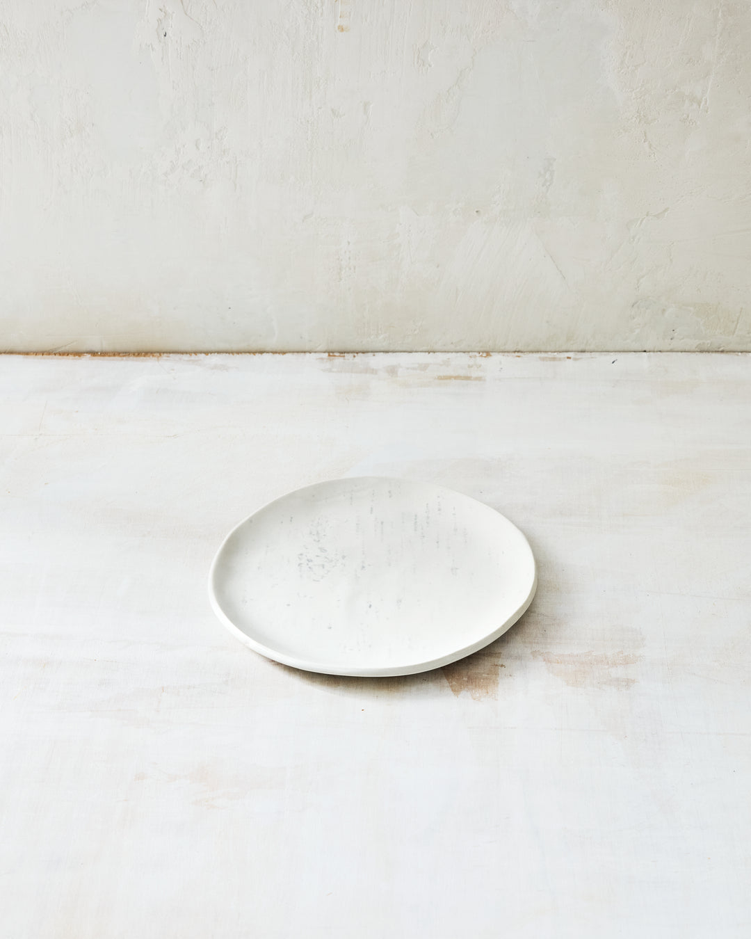 A handmade porcelain bread plate from DBO Home's Birch collection in Salt n Pepper glaze, with subtle birch bark texture, photographed at a low angle on a whitewashed surface