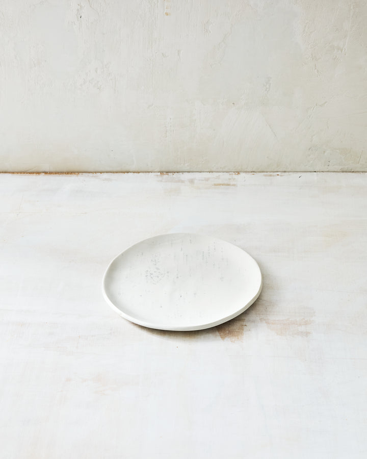 A handmade porcelain bread plate from DBO Home's Birch collection in Salt n Pepper glaze, with subtle birch bark texture, photographed at a low angle on a whitewashed surface