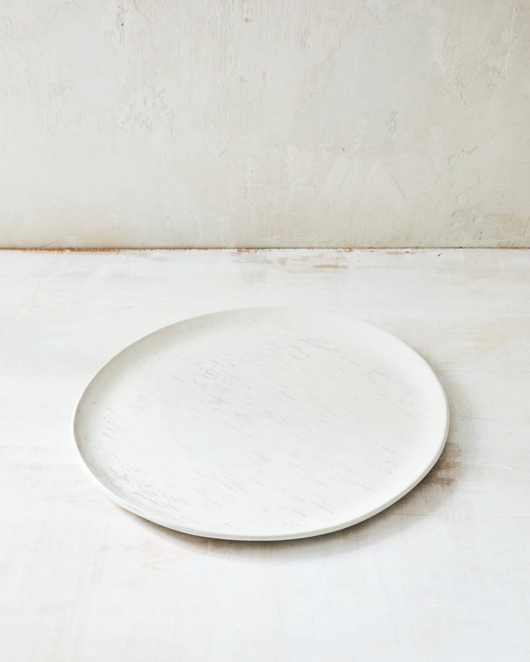 A handmade porcelain dinner plate from DBO Home's Birch collection in Salt n Pepper glaze, with birch bark-impressed surface texture, photographed at a low angle on a whitewashed surface