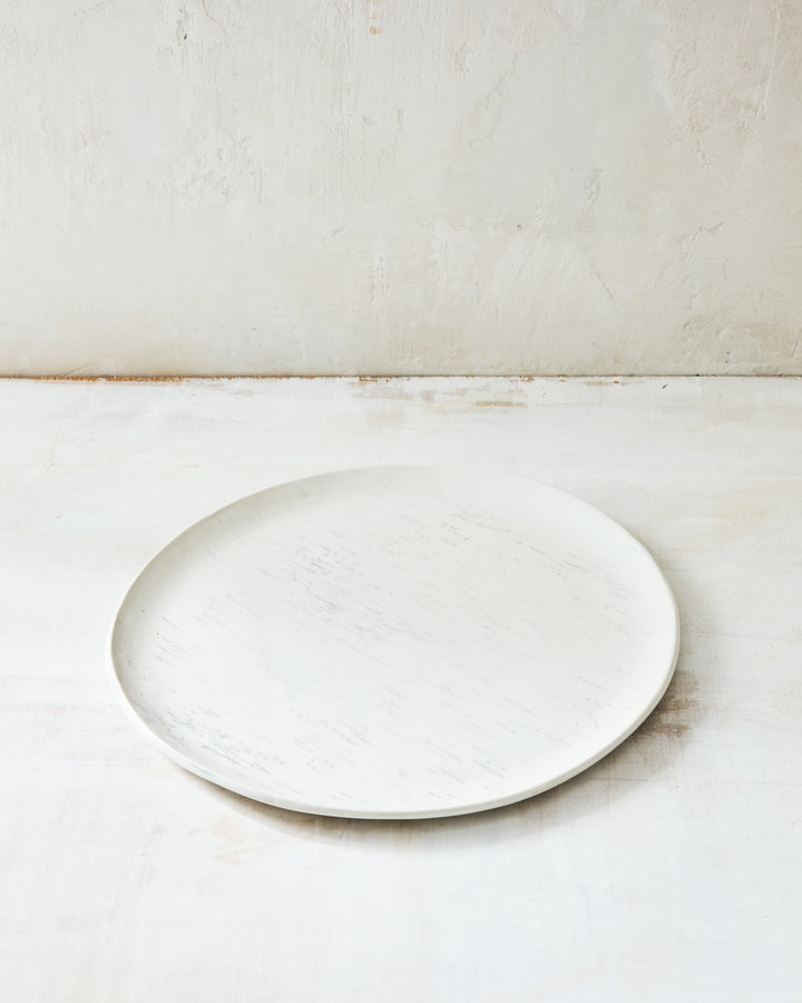 A handmade porcelain dinner plate from DBO Home's Birch collection in Salt n Pepper glaze, with birch bark-impressed surface texture, photographed at a low angle on a whitewashed surface