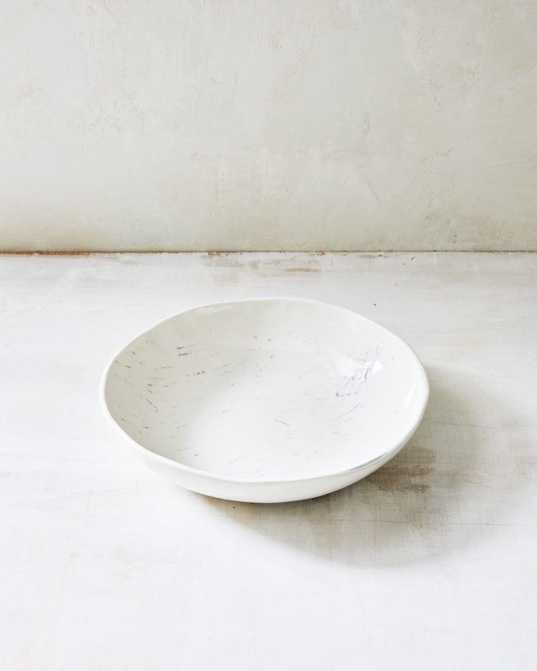 A wide, shallow artisan ceramic serving bowl from DBO Home's Birch collection in Salt n Pepper glaze, with birch bark-impressed texture, photographed at a low angle on a whitewashed surface