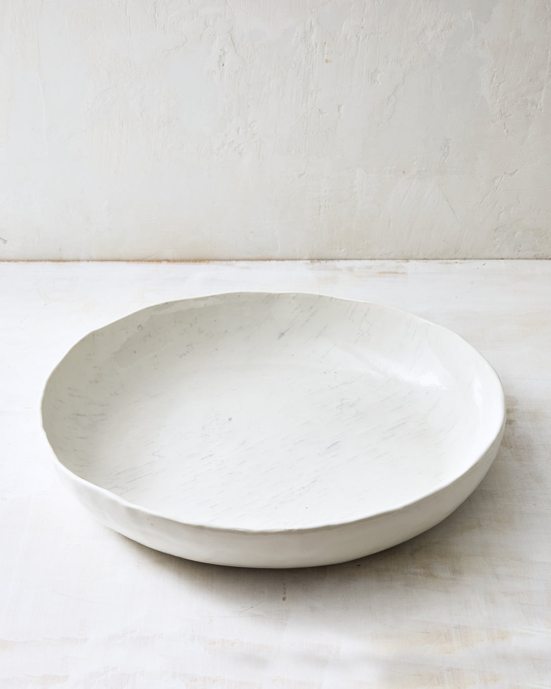 An oversized handmade porcelain bowl from DBO Home's Birch collection in Salt n Pepper glaze, with an organic rim and birch bark-impressed texture, photographed at a low angle on a whitewashed surface