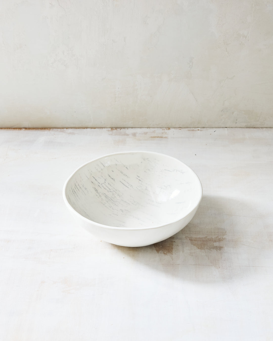 A deep, rounded artisan ceramic noodle bowl from DBO Home's Birch collection in Salt n Pepper glaze, with birch bark-impressed interior texture, photographed at a low angle on a whitewashed surface