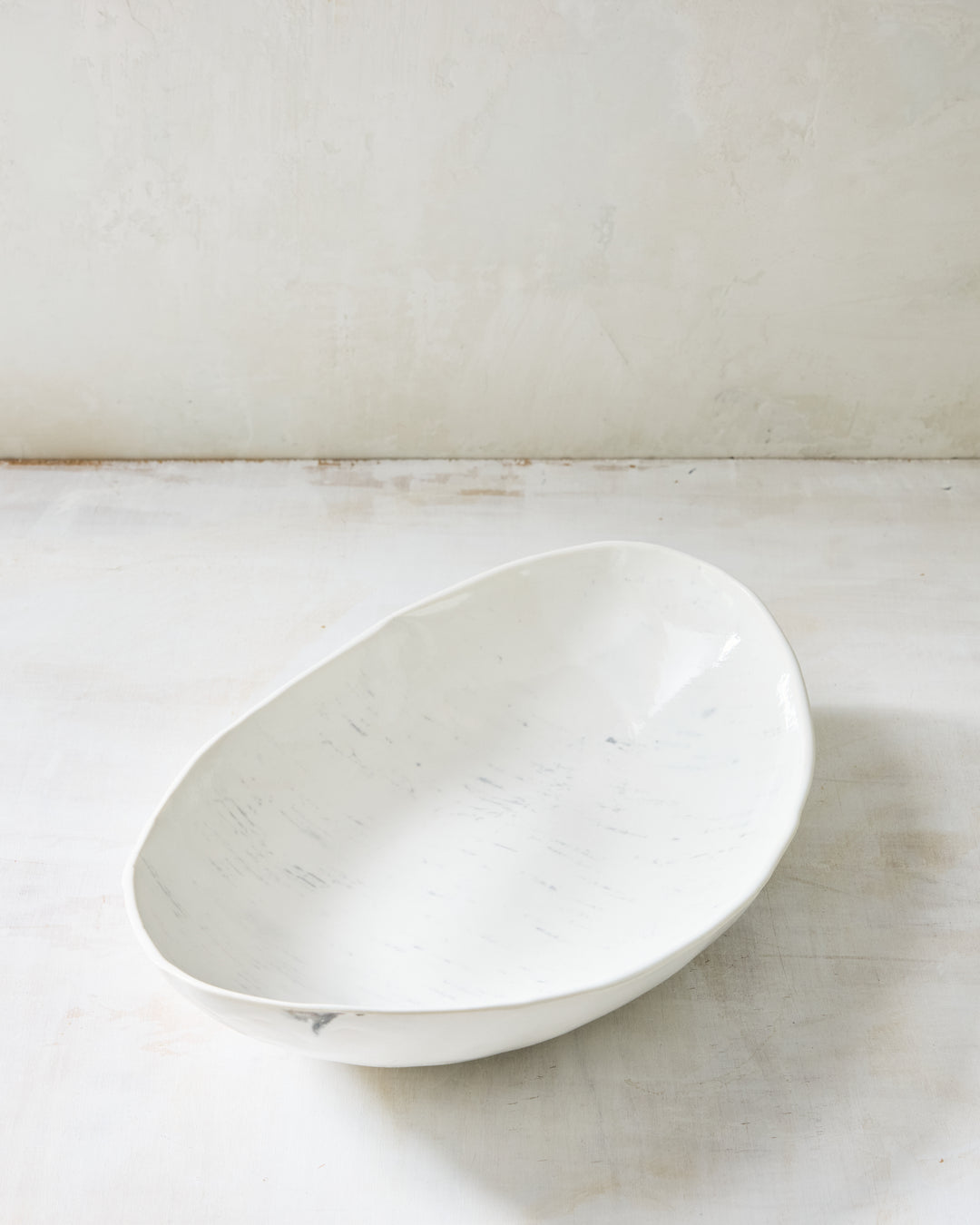 A large handmade porcelain oval serving bowl from DBO Home's Birch collection in Salt n Pepper glaze, with an organic asymmetric rim and birch bark-impressed texture, photographed at a low angle on a whitewashed surface
