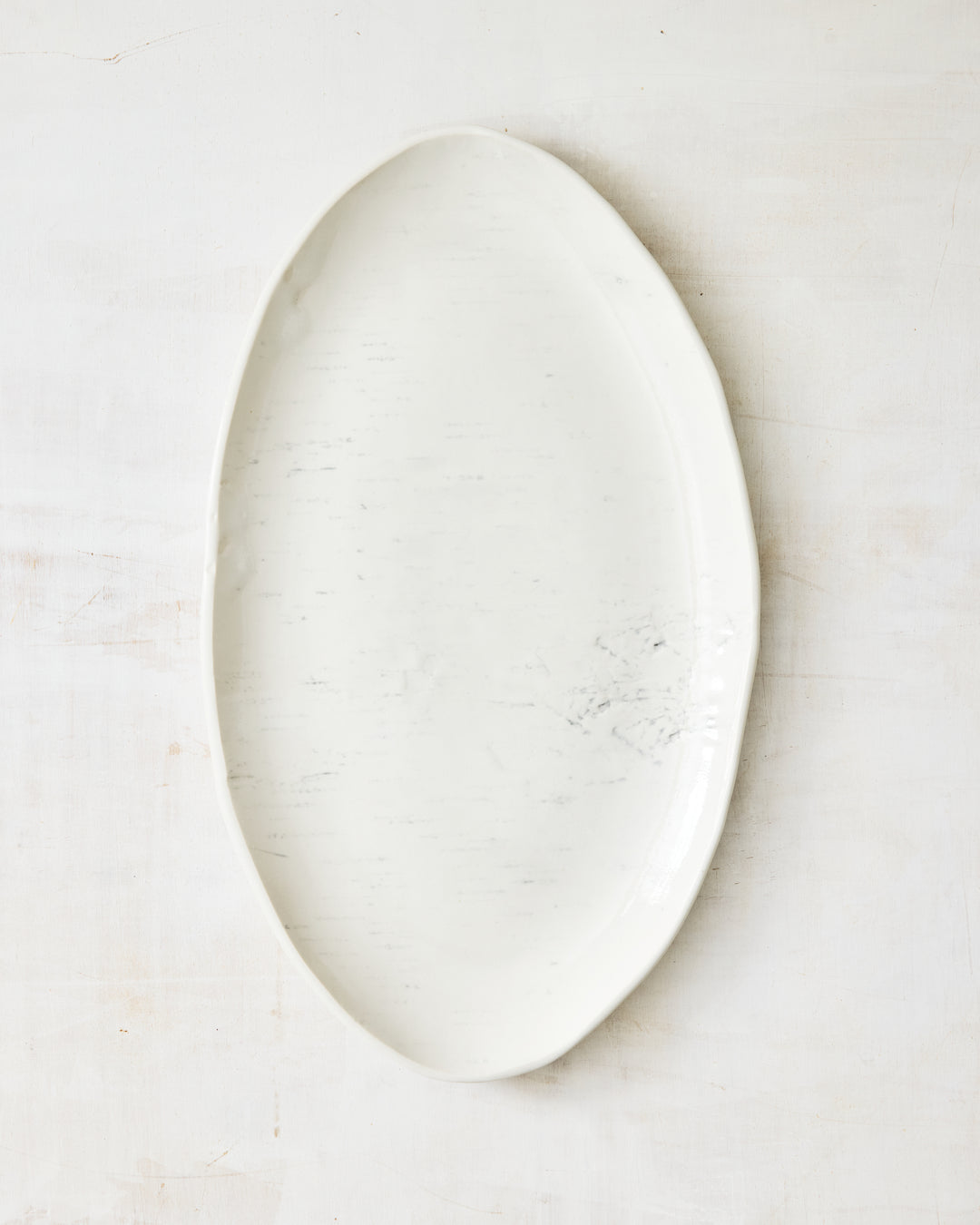 A large oval serving platter from DBO Home's Birch collection in Salt n Pepper glaze, handmade porcelain with an organic rim and birch bark-impressed texture, photographed overhead on a white painted wood surface