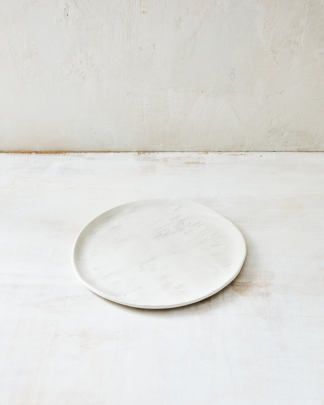 A handmade porcelain salad plate from DBO Home's Birch collection in Salt n Pepper glaze, with birch bark-impressed surface texture, photographed at a low angle on a whitewashed surface