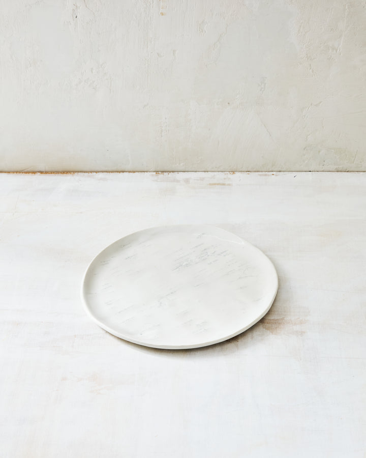 A handmade porcelain salad plate from DBO Home's Birch collection in Salt n Pepper glaze, with birch bark-impressed surface texture, photographed at a low angle on a whitewashed surface