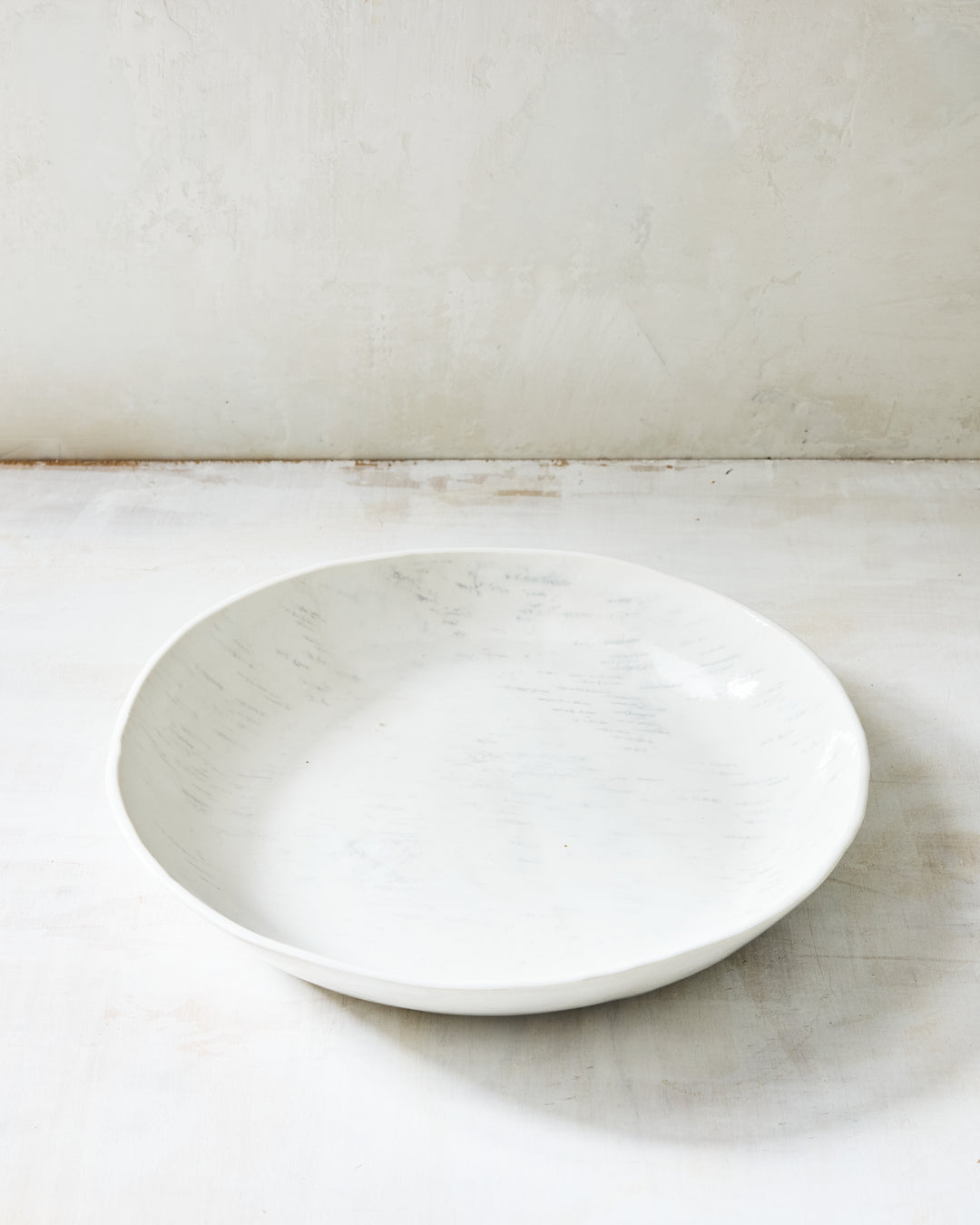A wide, shallow artisan ceramic serving bowl from DBO Home's Birch collection in Salt n Pepper glaze, with a gently curved rim and birch bark-impressed texture, photographed at a low angle on a whitewashed surface