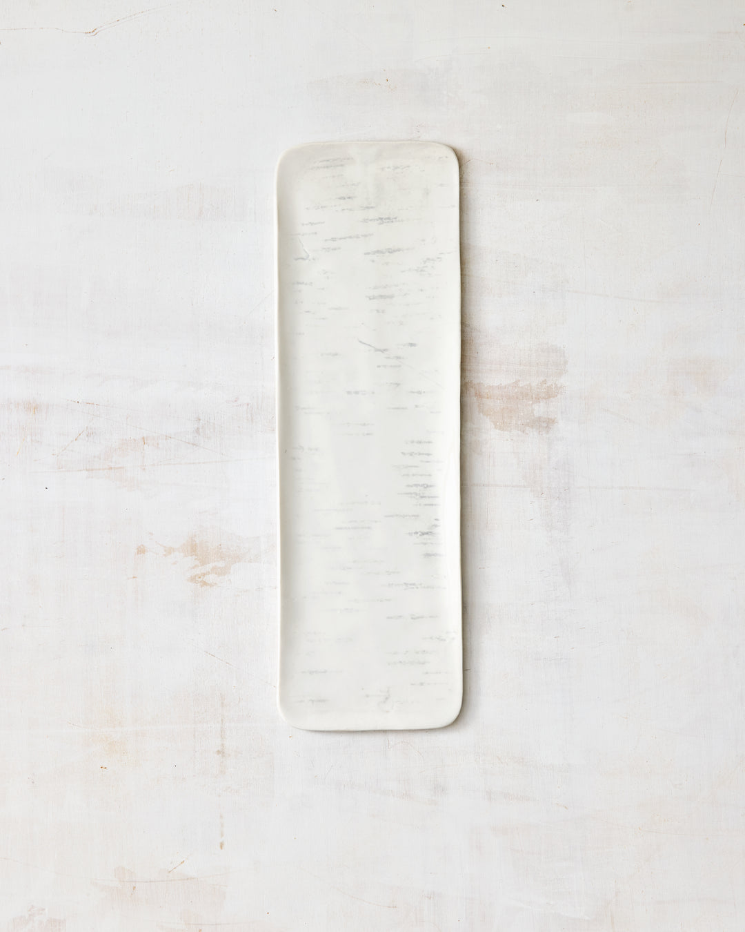 A tall, narrow artisan ceramic tray from DBO Home's Birch collection in Salt n Pepper glaze, with rounded corners and a prominently visible birch bark-impressed texture, photographed overhead on a white painted wood surface