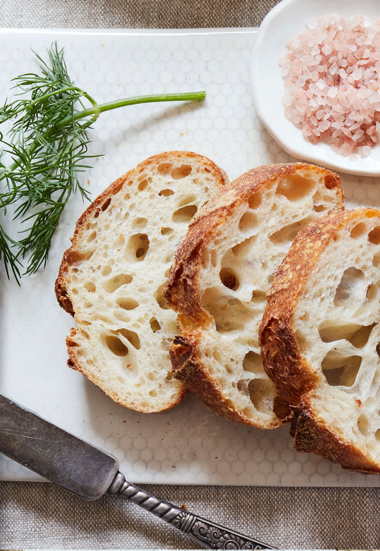 Freshly cut slices of crusty sourdough bread from Bourke Street Bakery on DBO Honeycomb Rectangular Serveware with a sprig of fresh dill and a vintage DBO dipping bowl full of pink Himalayan sea salt