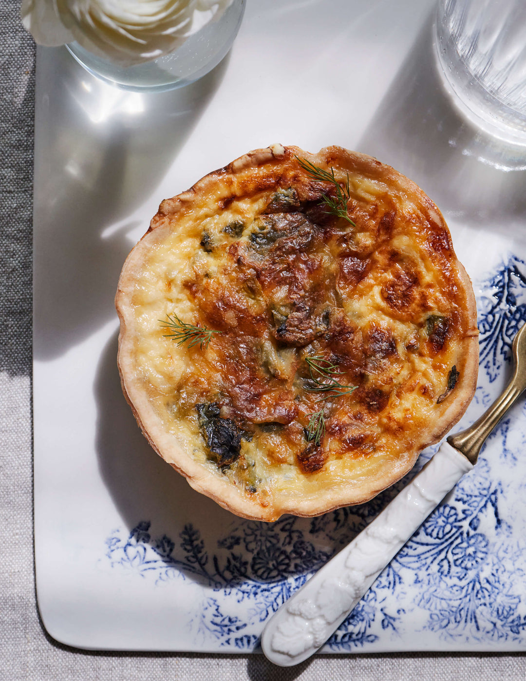 Mini quiche topped with fresh dill from Bourke Street Bakery on a DBO Home Kashmir Cheese Board with vintage glassware and white enamel fork