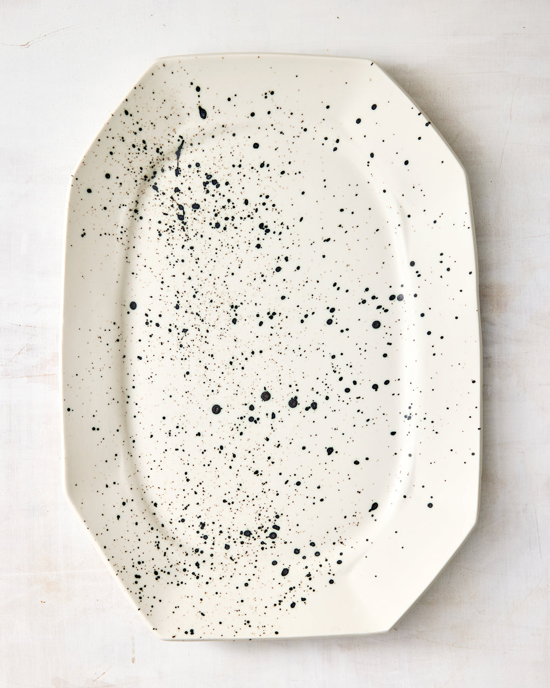 Formale Platter by DBO HOME in natural porcelain, finished with an expressive black speckle glaze. The clean, structured form contrasts beautifully with the organic splatter pattern.