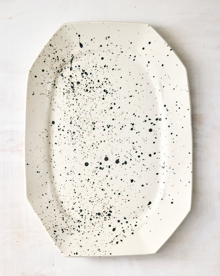 Formale Platter by DBO HOME in natural porcelain, finished with an expressive black speckle glaze. The clean, structured form contrasts beautifully with the organic splatter pattern.