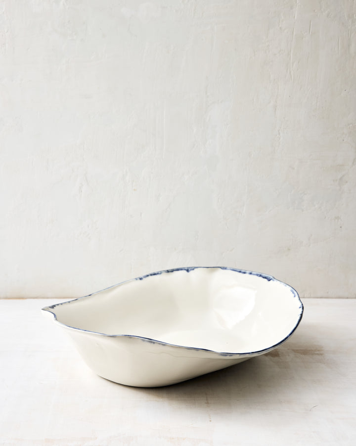Angled view of the DBO HOME Formale Serving Bowl in porcelain with indigo glaze. Hand-formed edges and a soft sheen add understated beauty to this refined tabletop piece.