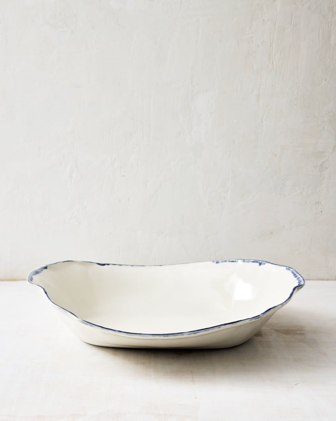 DBO HOME Formale Serving Bowl in porcelain with a brushed indigo rim. A softly fluted form and minimal profile lend quiet character to this artisan serving piece.