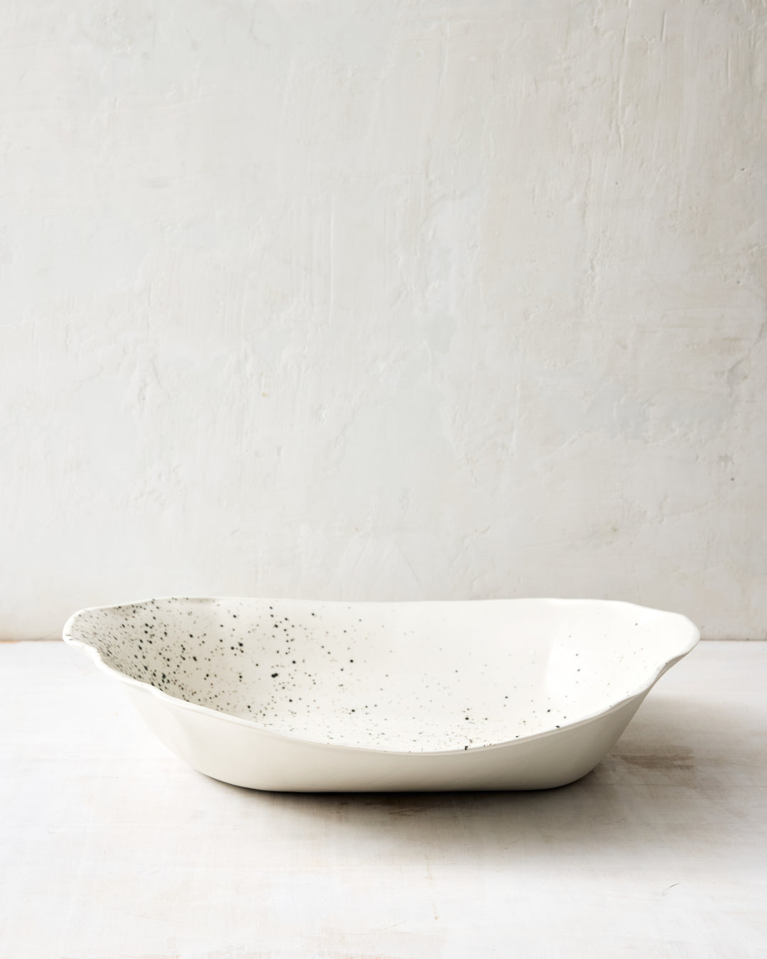 DBO HOME Formale Serving Bowl in natural porcelain with a black speckle glaze. The generous form and soft curves are framed by hand-shaped edges, blending expressive detail with refined function.