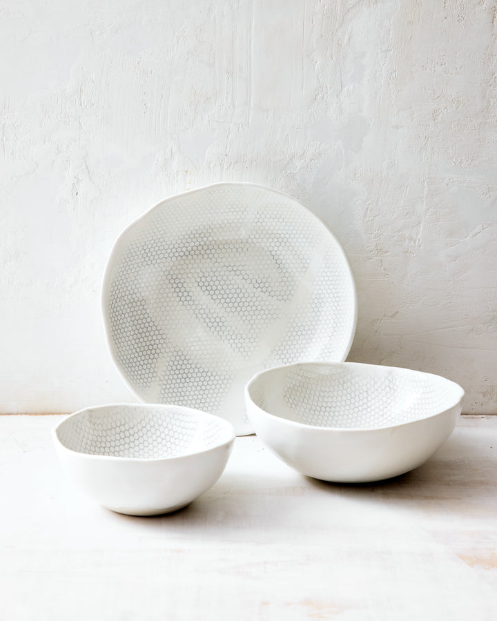 Three handmade porcelain bowls from DBO HOME's Honeycomb collection arranged together — small, medium, and large — all in a white gloss glaze with pale grey-inlaid honeycomb pattern, photographed against a whitewashed wall.