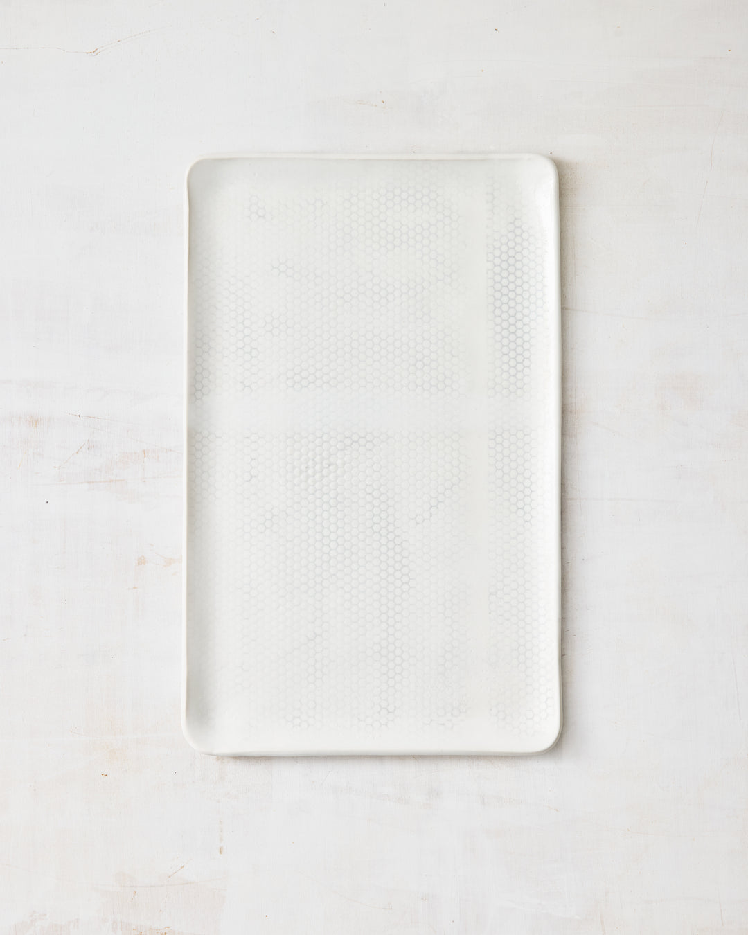 DBO HOME Honeycomb Large Platter in handmade porcelain with a white gloss glaze and pale grey-inlaid honeycomb texture, wide rectangular form with softly rounded corners, photographed overhead on a white painted wood surface.