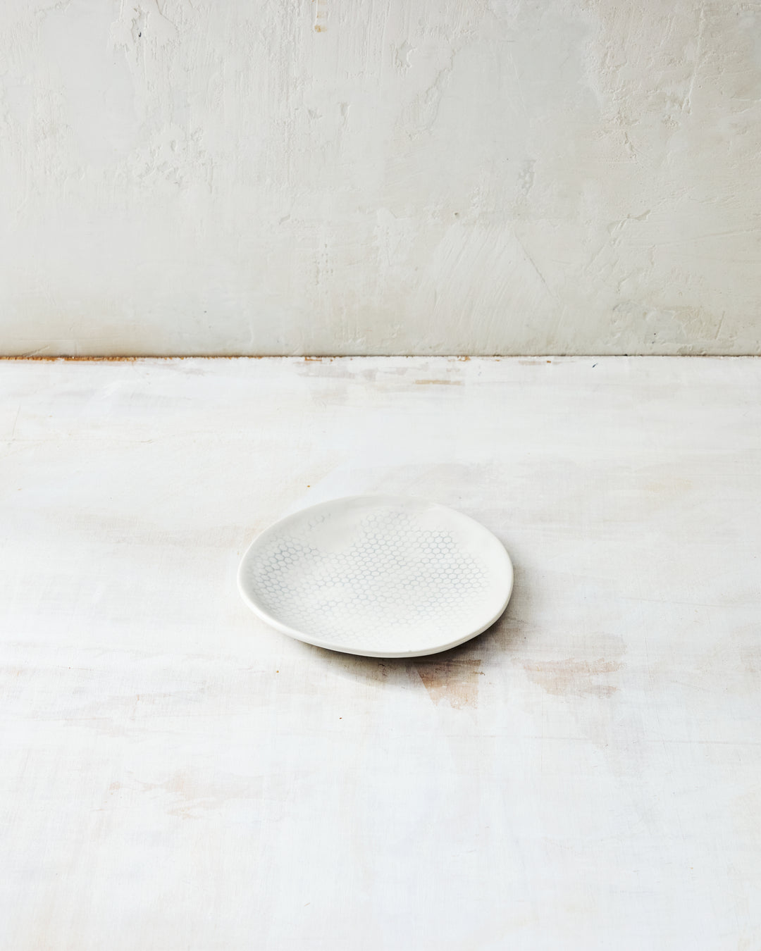 DBO HOME Honeycomb Lil Bowl in handmade porcelain with a white gloss glaze and pale grey-inlaid honeycomb texture, small shallow form, photographed at a low angle on a whitewashed surface.