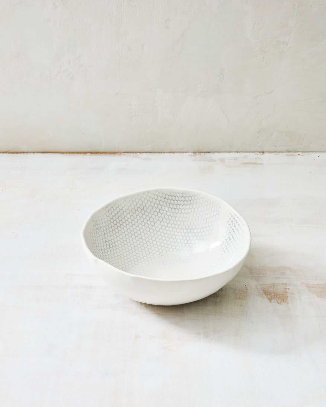 DBO HOME Honeycomb Noodle Bowl in handmade porcelain with a white gloss glaze and pale grey-inlaid honeycomb texture, photographed at a low angle on a whitewashed surface.