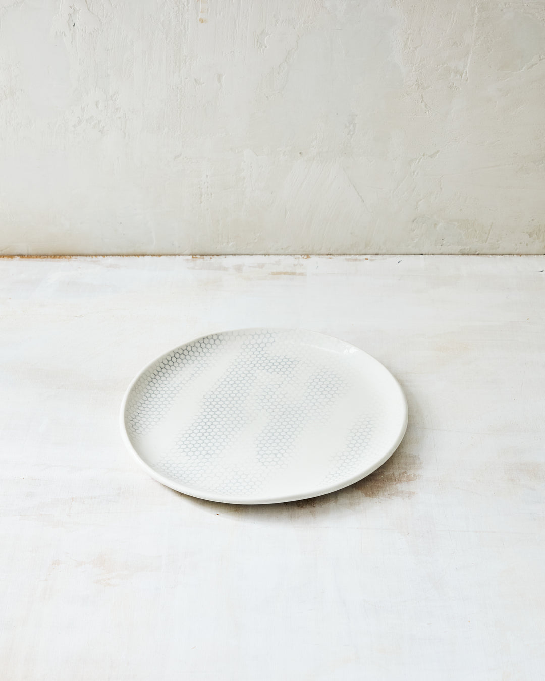 DBO HOME Honeycomb Salad Plate in handmade porcelain with a white gloss glaze and pale grey-inlaid honeycomb texture, photographed at a low angle on a whitewashed surface.