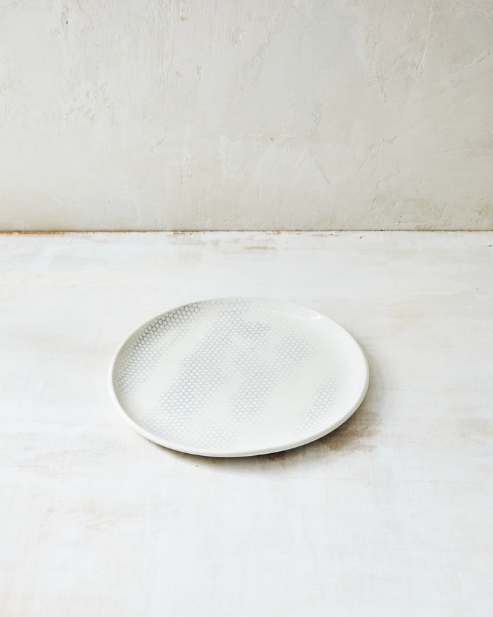 DBO HOME Honeycomb Salad Plate in handmade porcelain with a white gloss glaze and pale grey-inlaid honeycomb texture, photographed at a low angle on a whitewashed surface.