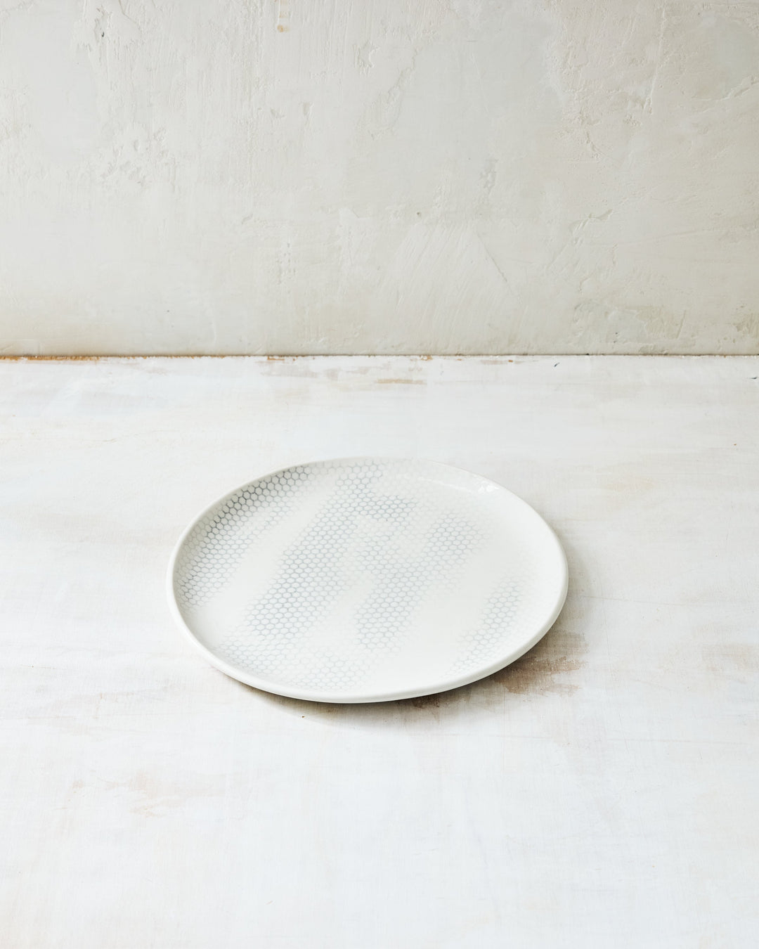 DBO HOME Honeycomb Salad Plate in handmade porcelain with a white gloss glaze and pale grey-inlaid honeycomb texture, photographed at a low angle on a whitewashed surface.