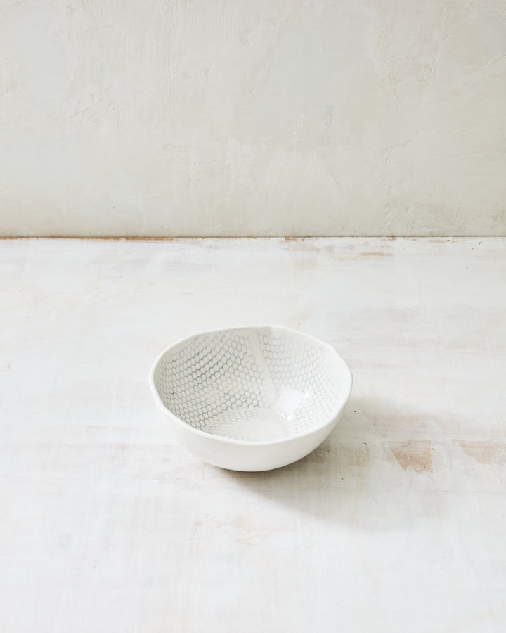 DBO HOME Honeycomb Soup Bowl in handmade porcelain with a white gloss glaze and pale grey-inlaid honeycomb texture, small and rounded, photographed at a low angle on a whitewashed surface.