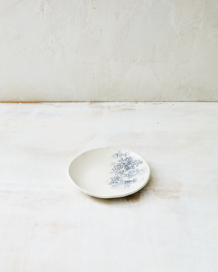 Handmade Kashmir lil bowl in white ceramic stoneware, featuring a delicate blue floral transfer pattern inspired by antique textiles, with a shallow, gently rounded form shown on a light, textured studio surface.