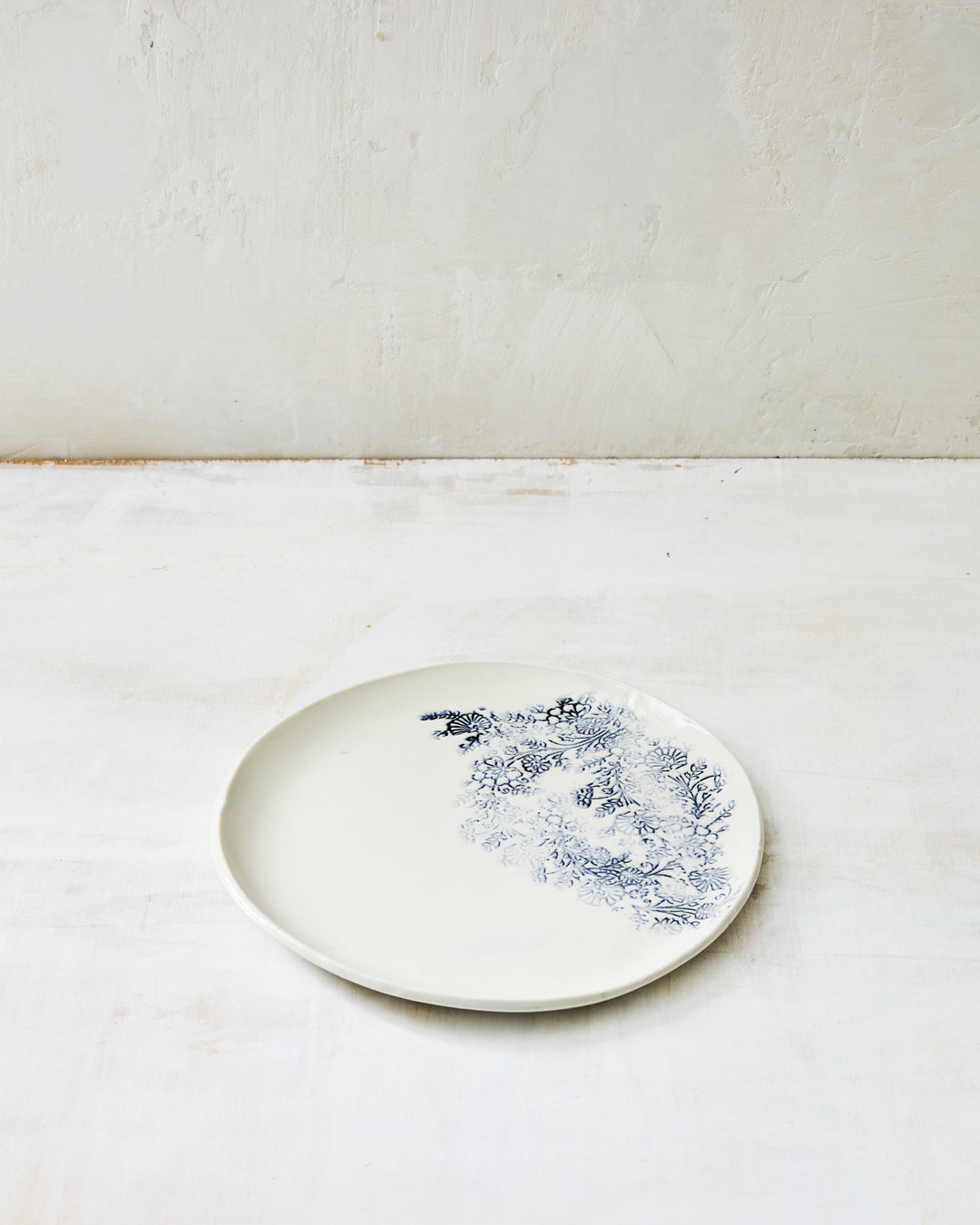 Kashmir salad plate in white porcelain with a relaxed blue indigo botanical motif along the rim, shown on a neutral studio surface.