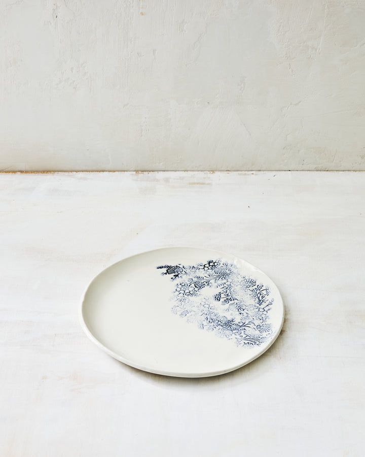 Kashmir salad plate in white porcelain with a relaxed blue indigo botanical motif along the rim, shown on a neutral studio surface.