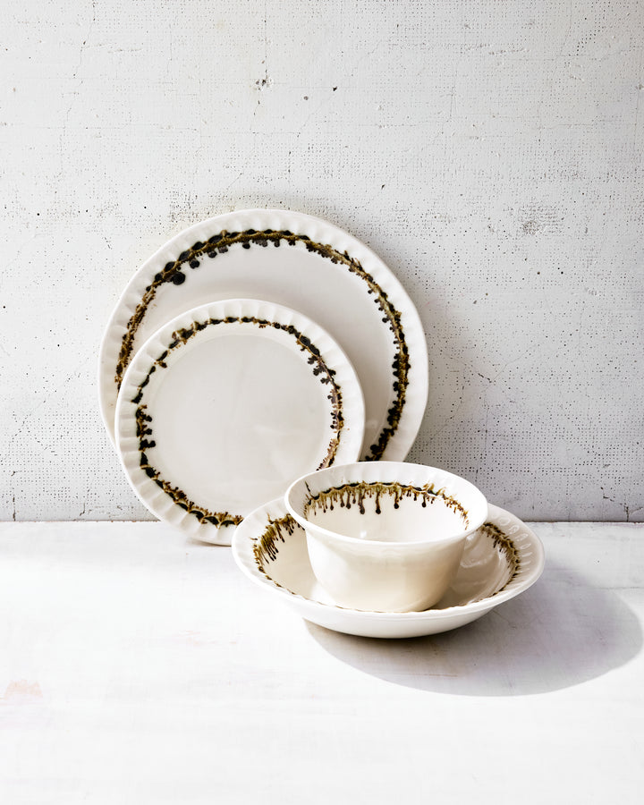 Stacked Nonna Dinnerware Set by DBO HOME in bronze glaze, including dinner and salad plates, wide bowl, and small bowl. Each piece is crafted from porcelain with a clear satin glaze and bronze-dipped edges, highlighting their organic shapes and sculptural silhouettes. Photographed in diffused light on a neutral surface.