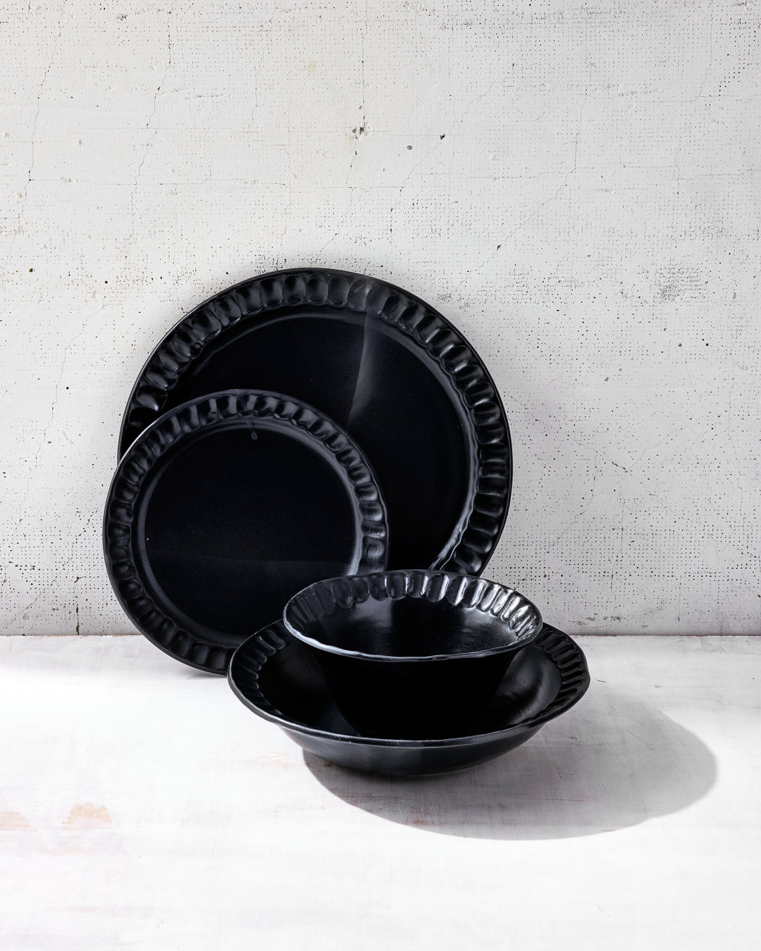 Stacked view of Nonna Dinnerware in Matte Black glaze from DBO HOME, showing the full place setting: dinner plate, salad plate, wide bowl, and small bowl. Each piece is hand-shaped from porcelain and finished in a deep, rich glaze, with subtle irregularities that speak to its handcrafted nature.