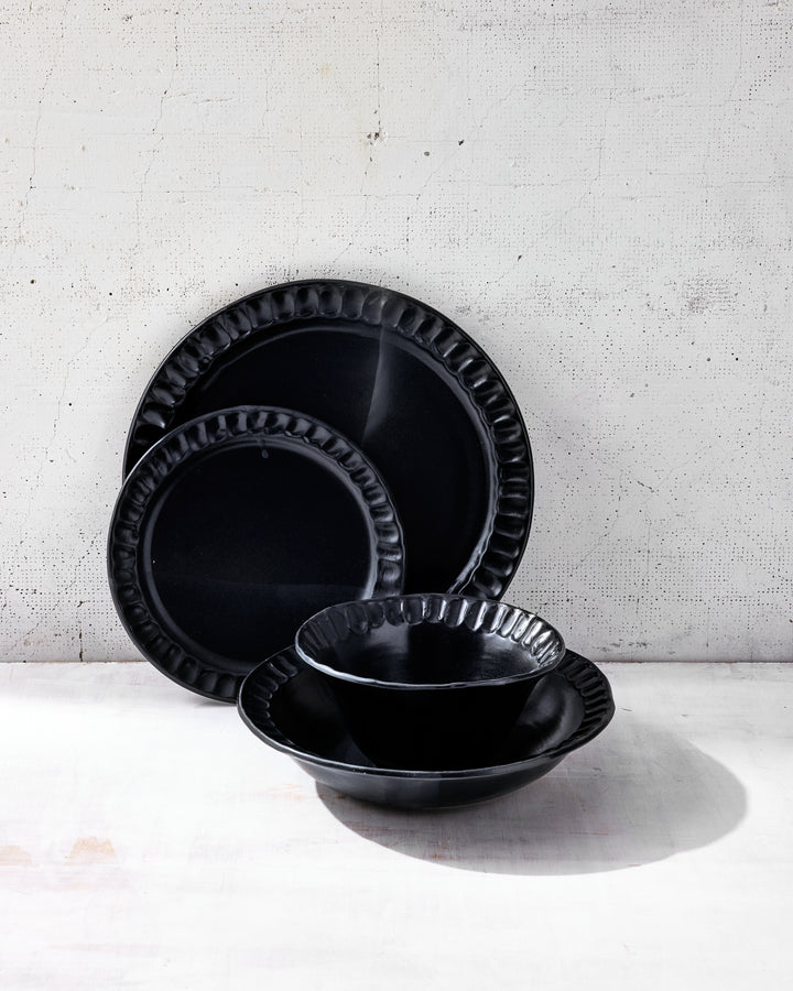 Stacked view of Nonna Dinnerware in Matte Black glaze from DBO HOME, showing the full place setting: dinner plate, salad plate, wide bowl, and small bowl. Each piece is hand-shaped from porcelain and finished in a deep, rich glaze, with subtle irregularities that speak to its handcrafted nature.