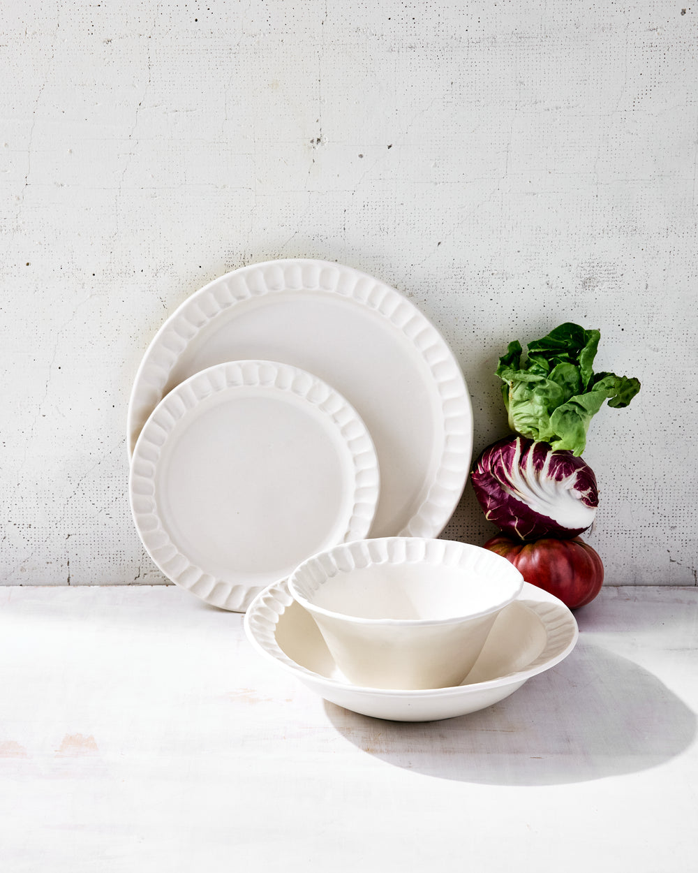 DBO HOME Nonna Dinnerware in luxe snowflake glaze, styled with heirloom vegetables on a light wood surface. The warm white porcelain glows softly under natural light, and the fluted rims catch gentle shadows. Includes a full place setting of dinnerware made for thoughtful everyday rituals.