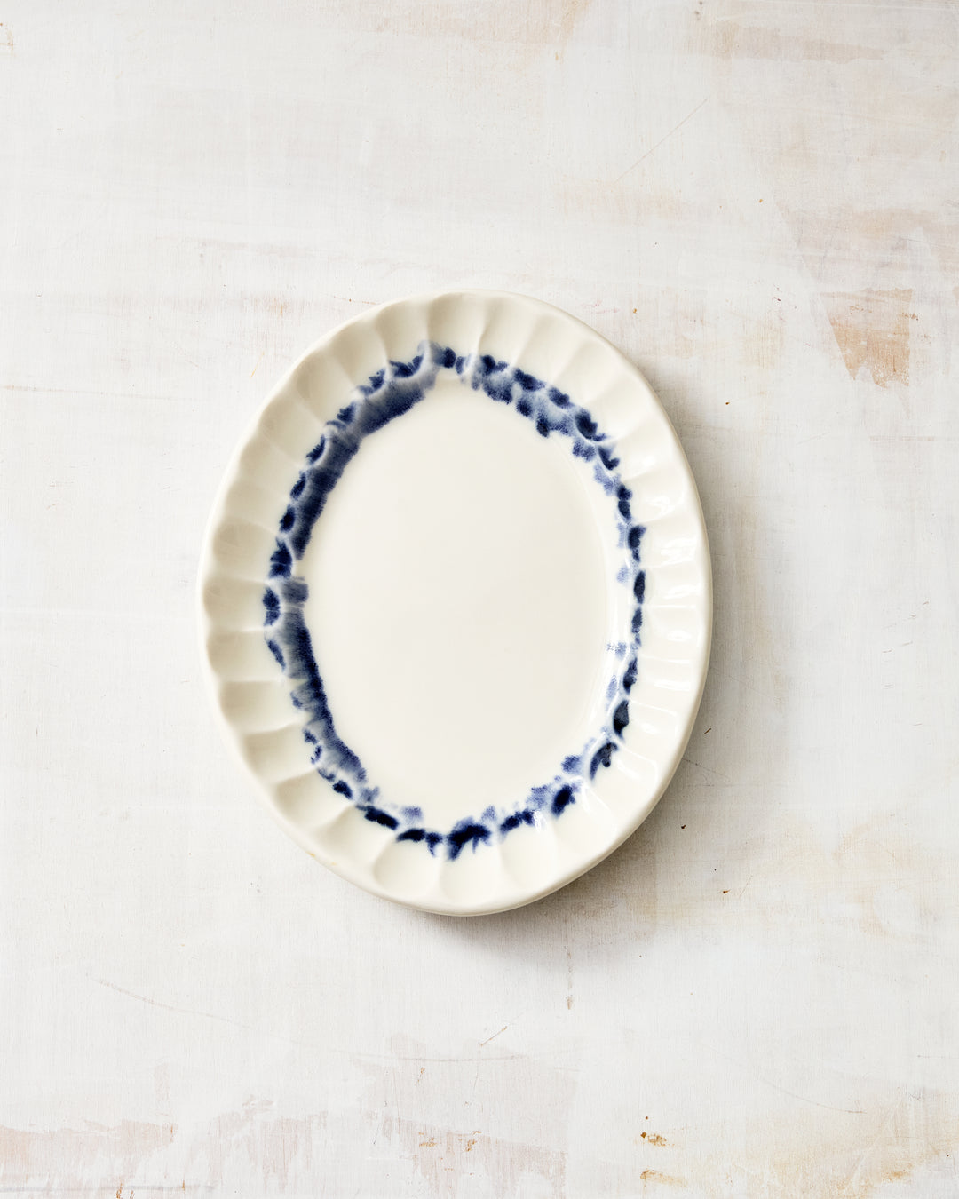 DBO HOME Nonna Oval Side Dish in Indigo glaze, handmade in white porcelain with a clear glossy finish and brushed cobalt rim that softly pools at the edges, photographed top-down