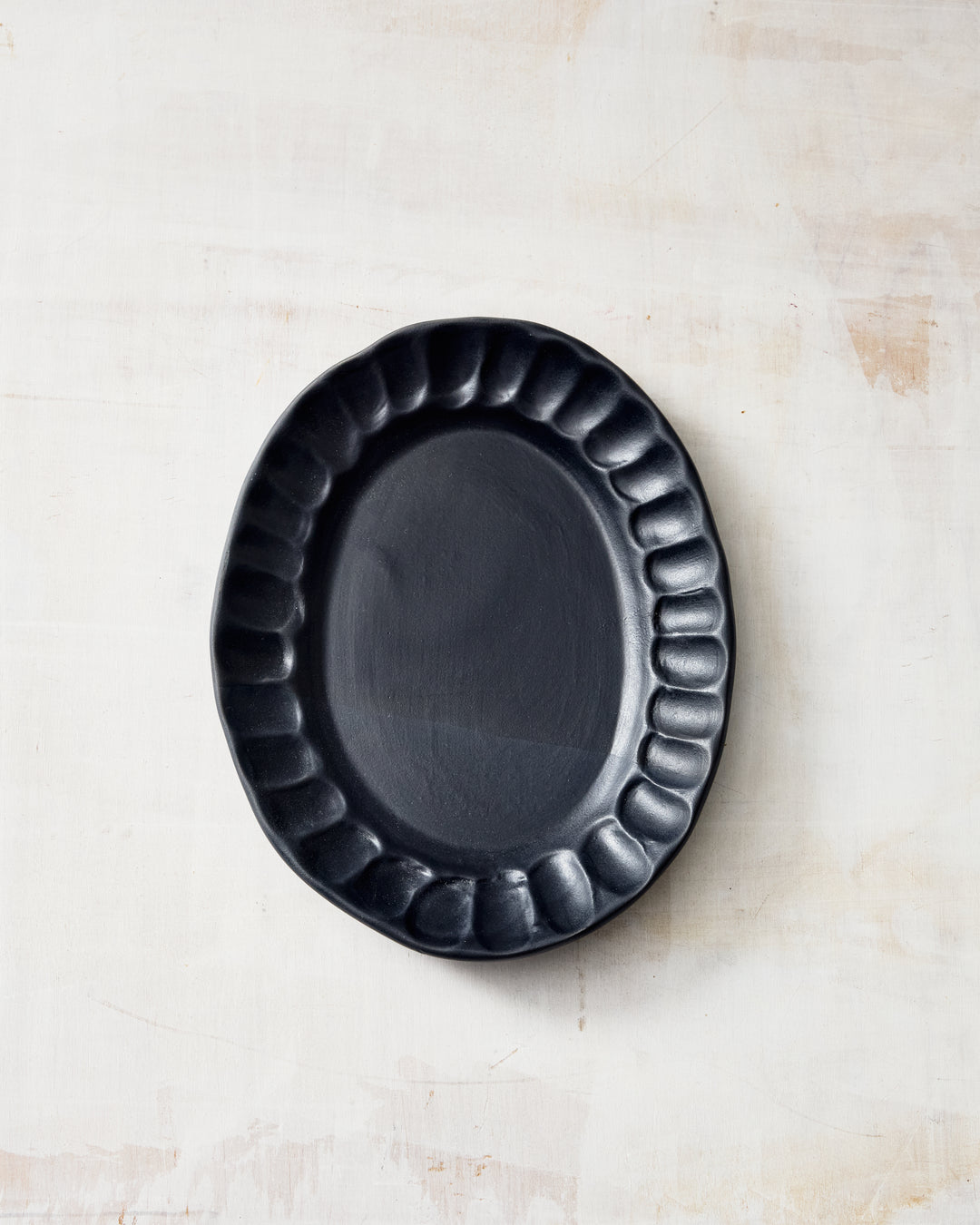 DBO HOME Nonna Oval Side Dish in Matte Black, showing deeply scalloped edges and a gently organic shape in a smooth satin black porcelain finish, styled on a light neutral surface