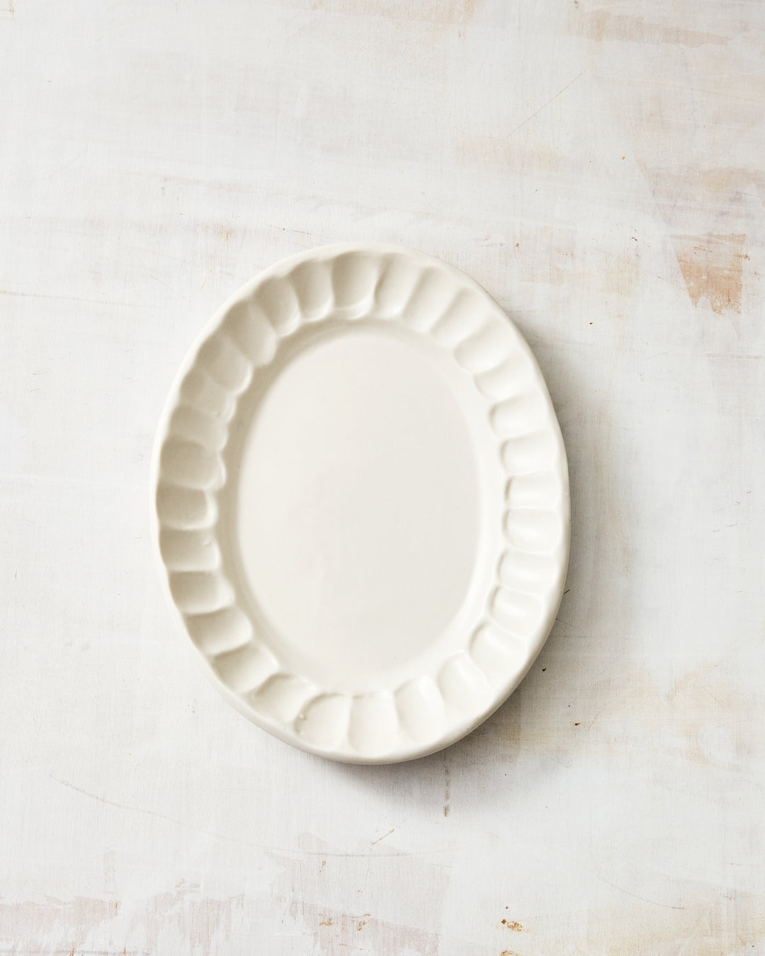DBO HOME Nonna Oval Side Dish in Snowflake glaze, handcrafted in creamy white porcelain with softly scalloped edges, photographed on a lightwashed wood surface