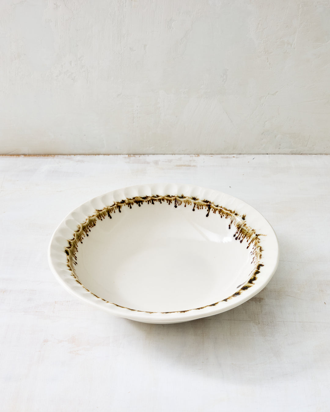 DBO HOME Nonna Pasta Bowl in creamy porcelain with hand-applied bronze glaze around the fluted rim. The clear base glaze allows subtle porcelain tones to shine through, while the bronze edge adds a painterly, earthy elegance.